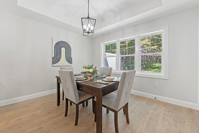 dining area with light hardwood / wood-style floors, a notable chandelier, and a raised ceiling