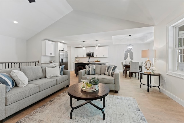 living room featuring lofted ceiling, sink, and light hardwood / wood-style flooring