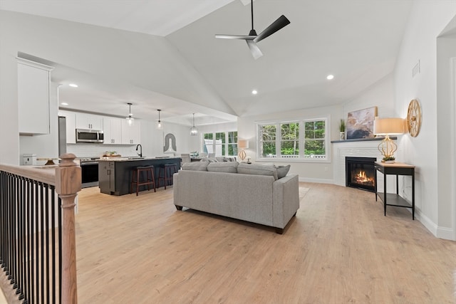 living room featuring ceiling fan, sink, light wood-type flooring, and a fireplace