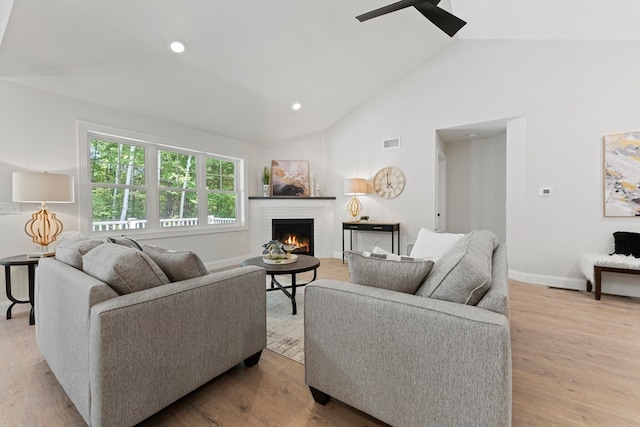 living room featuring high vaulted ceiling, a fireplace, light hardwood / wood-style floors, and ceiling fan