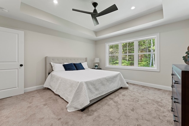 bedroom featuring light colored carpet, a raised ceiling, and ceiling fan