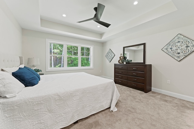 carpeted bedroom with ceiling fan and a tray ceiling