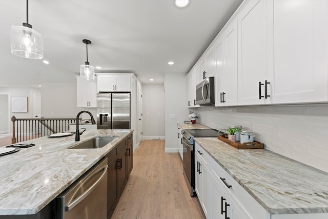 kitchen with appliances with stainless steel finishes, sink, hanging light fixtures, white cabinetry, and a kitchen island with sink