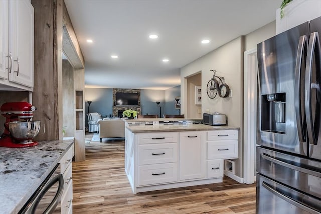 kitchen featuring stainless steel fridge, dishwasher, a fireplace, light hardwood / wood-style floors, and white cabinets