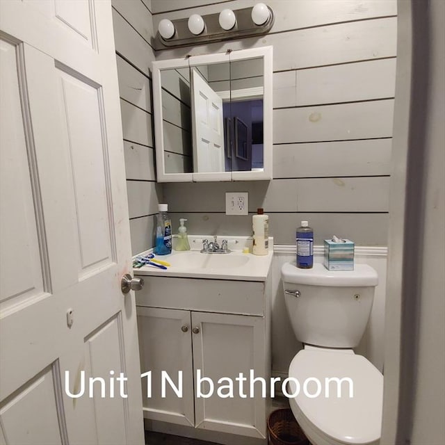 bathroom with vanity, wooden walls, and toilet