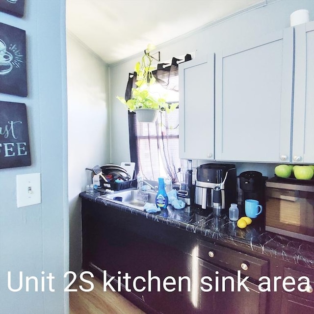 kitchen with crown molding, white cabinets, wood finished floors, and a sink