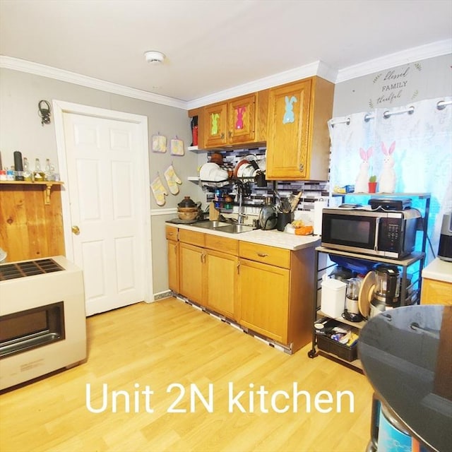 kitchen featuring light wood-style flooring, ornamental molding, light countertops, stainless steel microwave, and brown cabinets