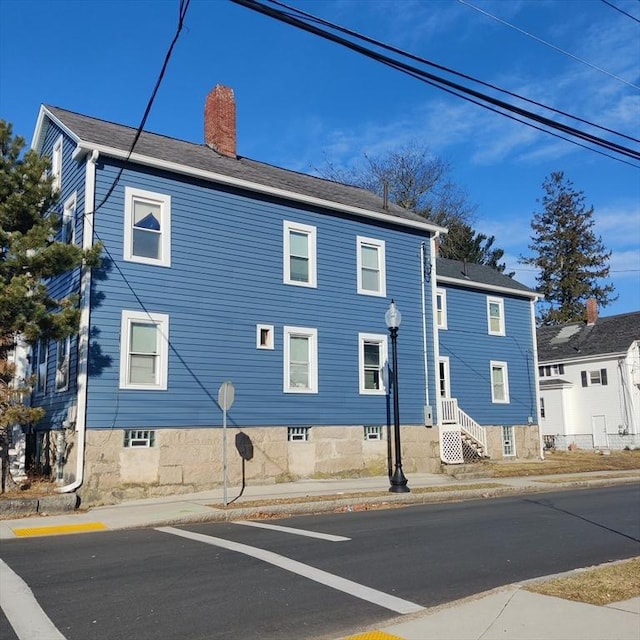 view of side of home with roof with shingles and a chimney