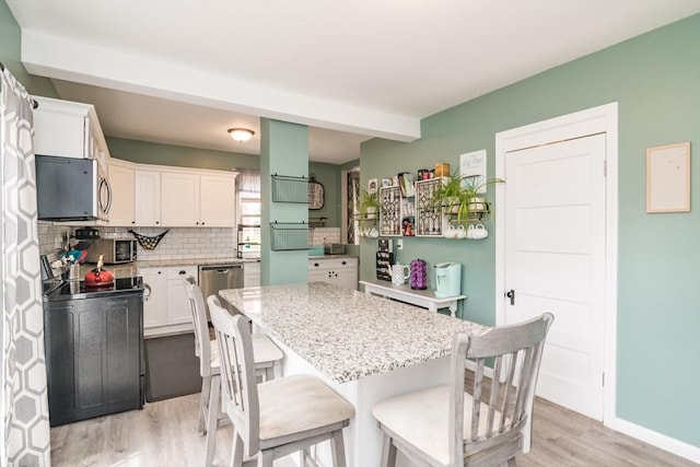 61 Fairfield Ave, Holyoke, MA 01040 - kitchen with light wood-type flooring, backsplash, white cabinetry, a kitchen island, and light stone countertops