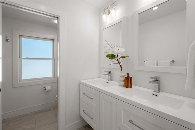 bathroom with double vanity, toilet, baseboards, and a sink