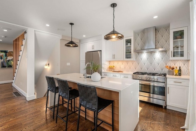 kitchen featuring visible vents, a kitchen island with sink, dark wood-style flooring, appliances with stainless steel finishes, and wall chimney range hood