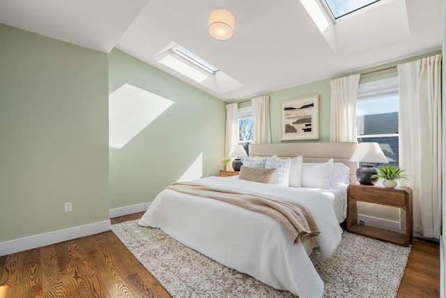 bedroom with baseboards, vaulted ceiling with skylight, and wood finished floors