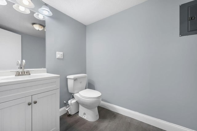 bathroom featuring wood-type flooring, toilet, vanity, electric panel, and a textured ceiling