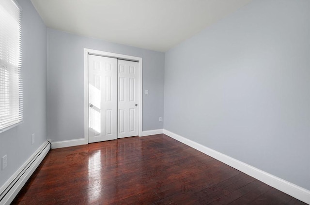 unfurnished bedroom with dark hardwood / wood-style flooring, a baseboard radiator, a closet, and multiple windows