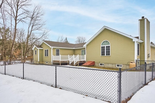 snow covered rear of property featuring a fenced backyard and a chimney