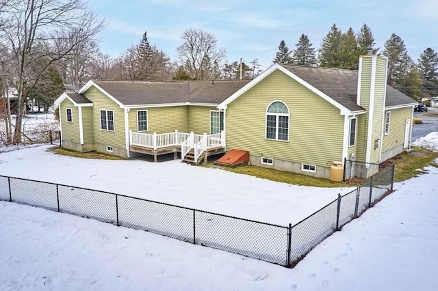 snow covered back of property featuring a wooden deck, a chimney, and fence