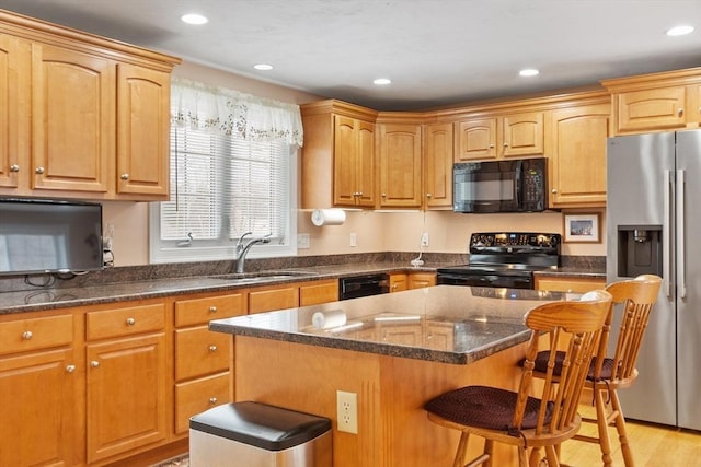 kitchen with a center island, a breakfast bar, dark stone counters, black appliances, and a sink