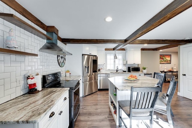 kitchen featuring open shelves, a sink, stainless steel appliances, beamed ceiling, and wall chimney exhaust hood