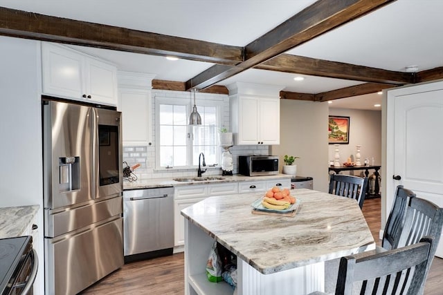 kitchen featuring backsplash, wood finished floors, white cabinets, stainless steel appliances, and a sink