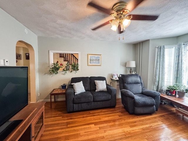 living area with a textured ceiling, light wood-style floors, arched walkways, and a ceiling fan