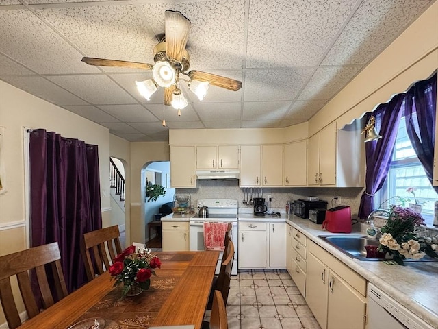 kitchen featuring white appliances, a sink, a paneled ceiling, under cabinet range hood, and arched walkways