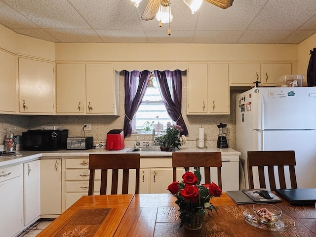 kitchen featuring freestanding refrigerator, a sink, black microwave, a drop ceiling, and light countertops