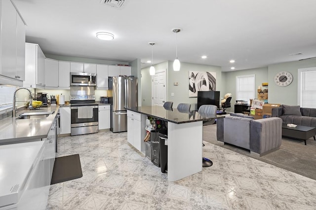 kitchen featuring appliances with stainless steel finishes, a kitchen island, sink, decorative light fixtures, and white cabinetry