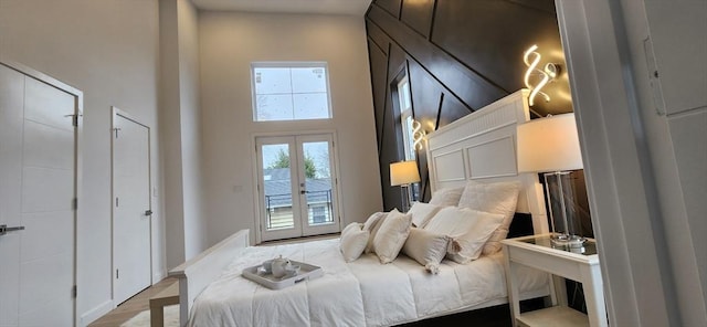 bedroom featuring access to exterior, a high ceiling, wood finished floors, and french doors