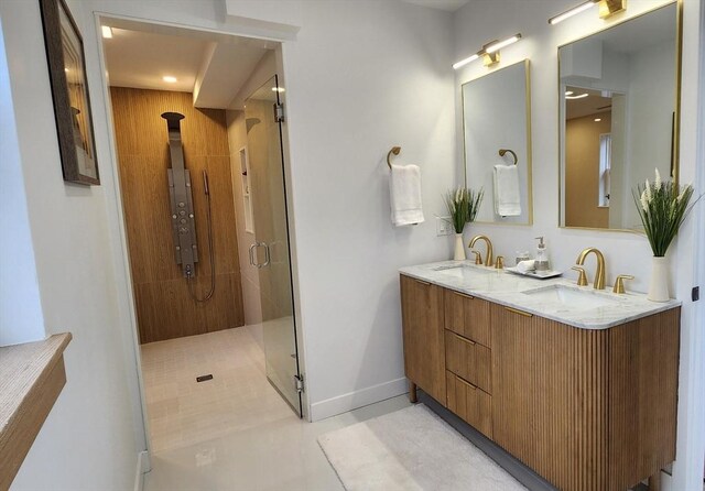 full bath with a stall shower, a sink, baseboards, and double vanity