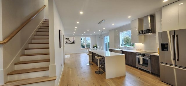 kitchen featuring modern cabinets, a kitchen island, stainless steel appliances, light countertops, and wall chimney range hood