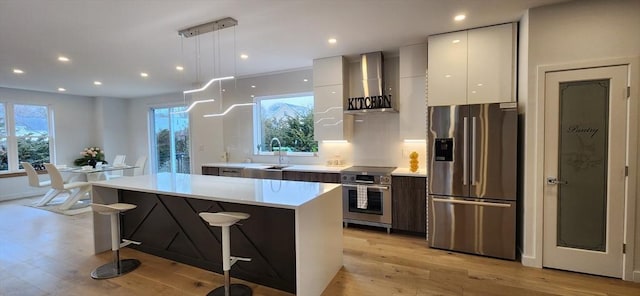 kitchen with modern cabinets, appliances with stainless steel finishes, a center island, wall chimney range hood, and white cabinetry