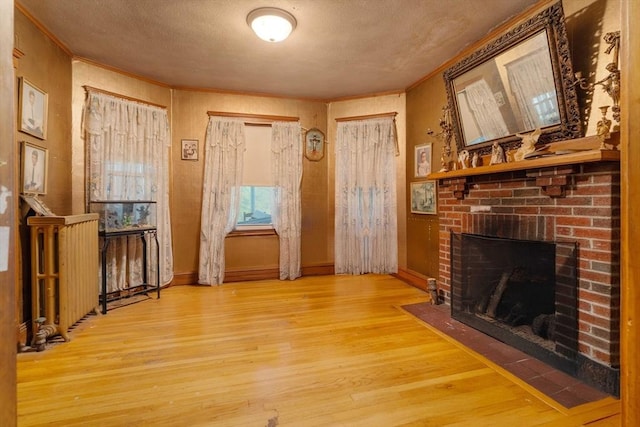 unfurnished living room with wood finished floors, ornamental molding, a brick fireplace, baseboards, and a textured ceiling