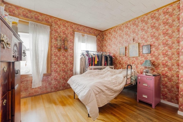 bedroom featuring wood finished floors, wallpapered walls, and crown molding