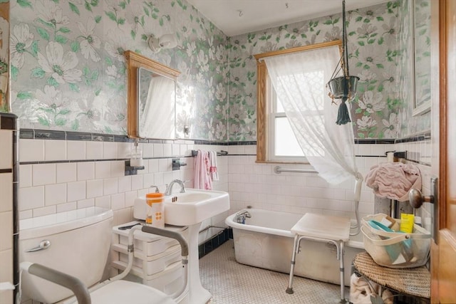 bathroom with wallpapered walls, a tub to relax in, toilet, a wainscoted wall, and tile walls