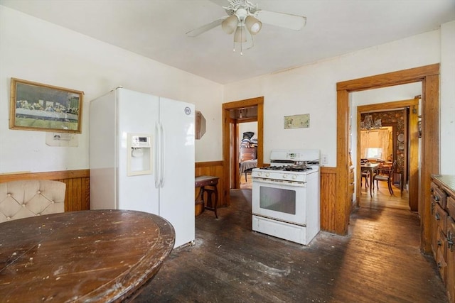 kitchen with white appliances, wainscoting, dark wood-type flooring, a ceiling fan, and wood walls