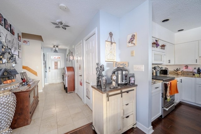 kitchen with stone counters, stainless steel range, white microwave, a textured ceiling, and baseboards