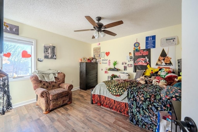 bedroom featuring ceiling fan, a textured ceiling, baseboards, and wood finished floors