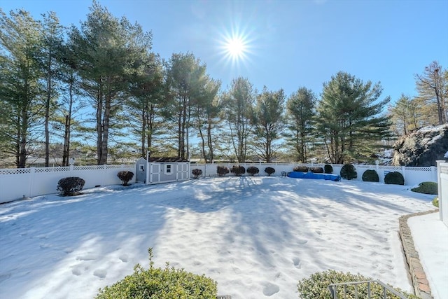 yard layered in snow featuring a fenced backyard, an outdoor structure, and a storage shed