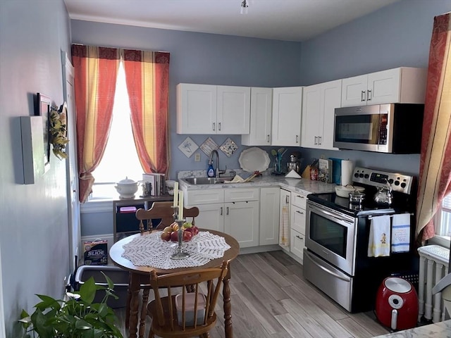 257 French St, Fall River, MA 02720 - kitchen with stainless steel appliances, a sink, white cabinets, and light wood-style flooring