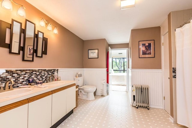 full bathroom featuring radiator heating unit, a wainscoted wall, double vanity, and toilet
