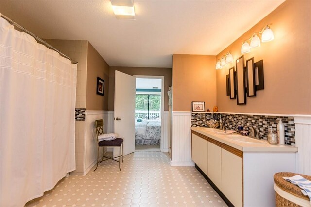 ensuite bathroom featuring a wainscoted wall, double vanity, and curtained shower