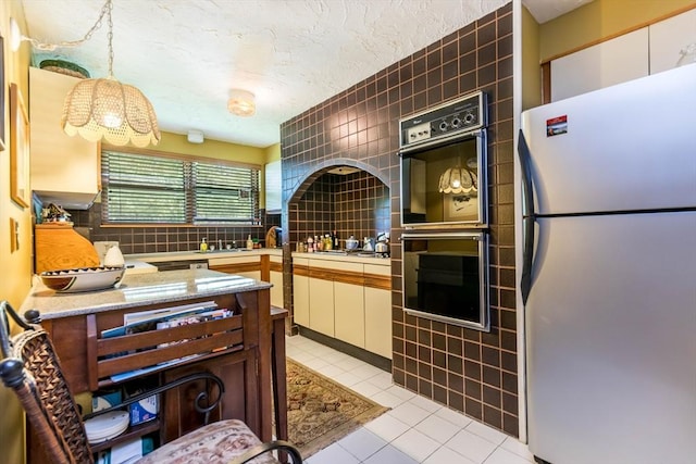 kitchen featuring freestanding refrigerator, multiple ovens, a textured ceiling, white cabinets, and light tile patterned floors