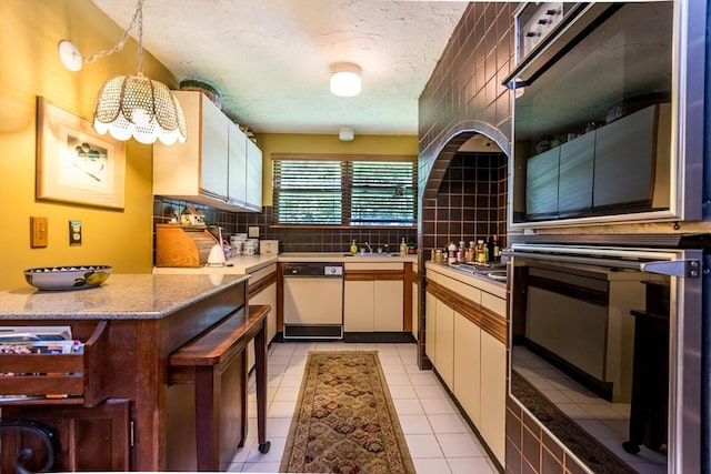 kitchen with oven, tasteful backsplash, light countertops, a chandelier, and white cabinetry