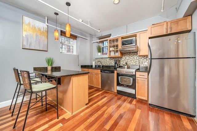 kitchen featuring appliances with stainless steel finishes, light wood-style floors, under cabinet range hood, tasteful backsplash, and a kitchen bar
