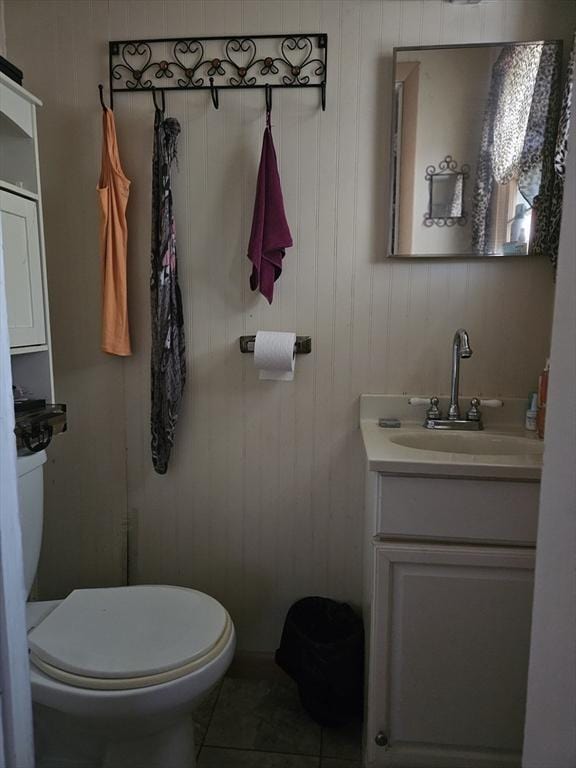 bathroom with toilet, tile patterned flooring, vanity, and wooden walls