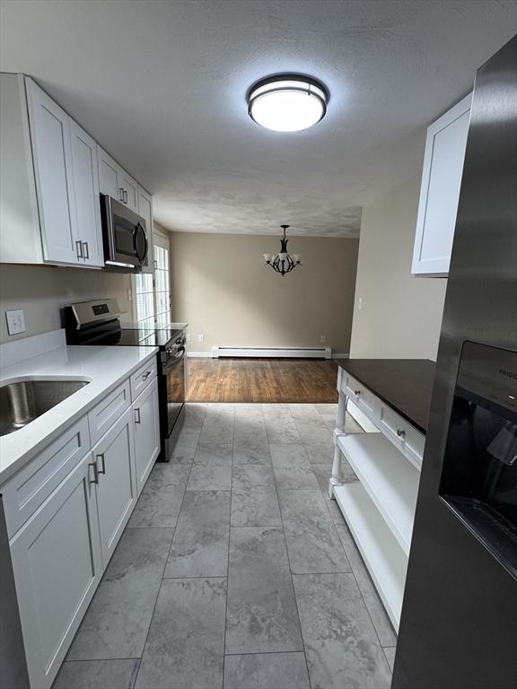 464 Church St, Raynham, MA 02767 - kitchen with stainless steel appliances, a baseboard radiator, white cabinets, and a chandelier