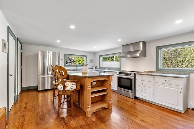 113 Bray St, Gloucester, MA 01930 - kitchen featuring appliances with stainless steel finishes, wall chimney range hood, open shelves, white cabinets, and light wood-style floors