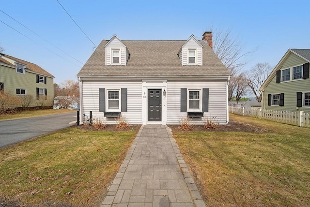 new england style home featuring roof with shingles, a chimney, a front yard, and fence