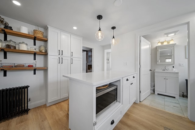 kitchen featuring radiator, light wood finished floors, light countertops, white cabinets, and stainless steel microwave