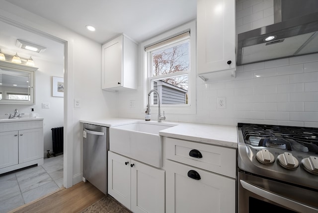 kitchen with a sink, decorative backsplash, stainless steel appliances, white cabinetry, and wall chimney range hood